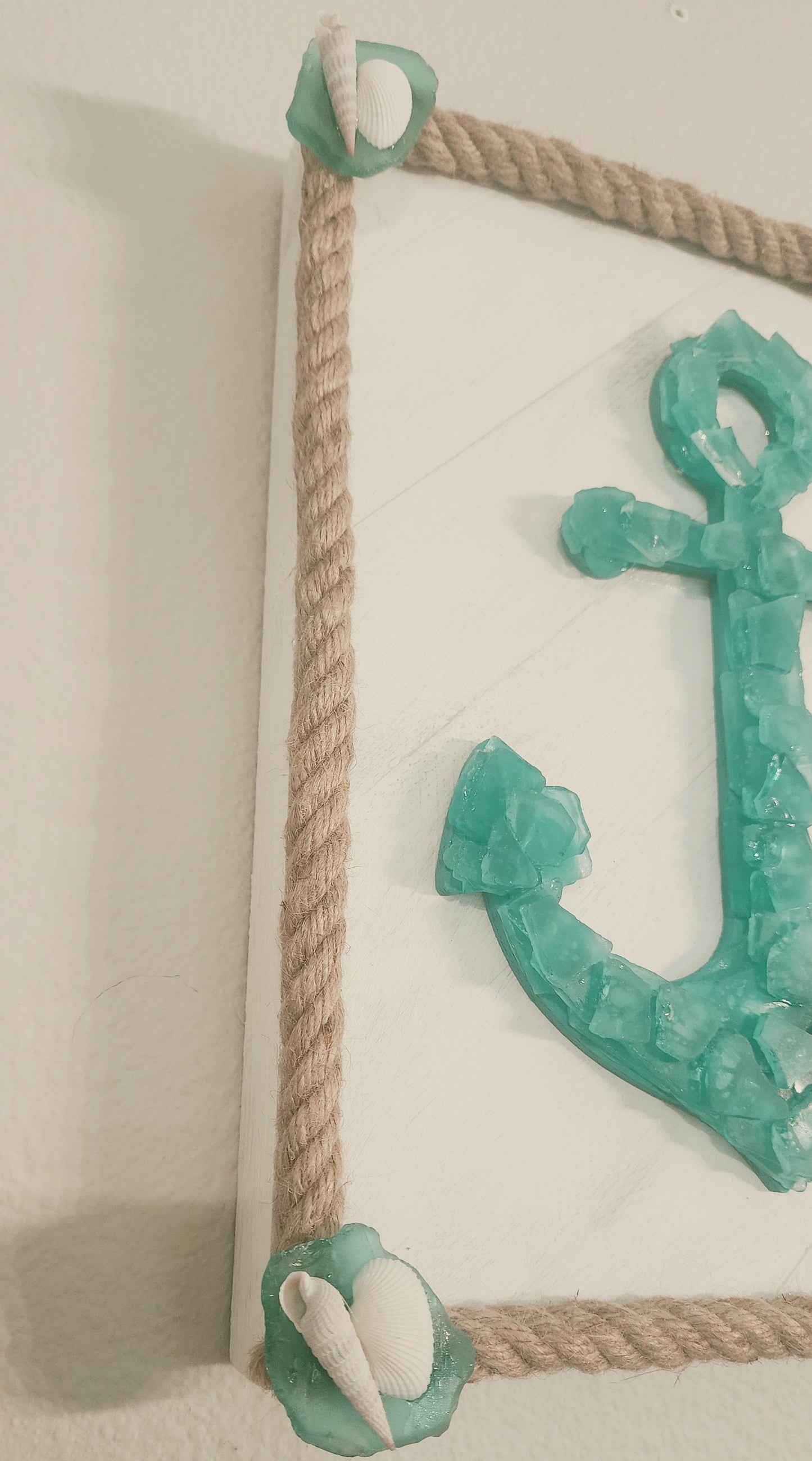 Sea glass anchor wall art in turquoise and white, surrounded with nautical jute rope, accented with a sand dollar and starfish.