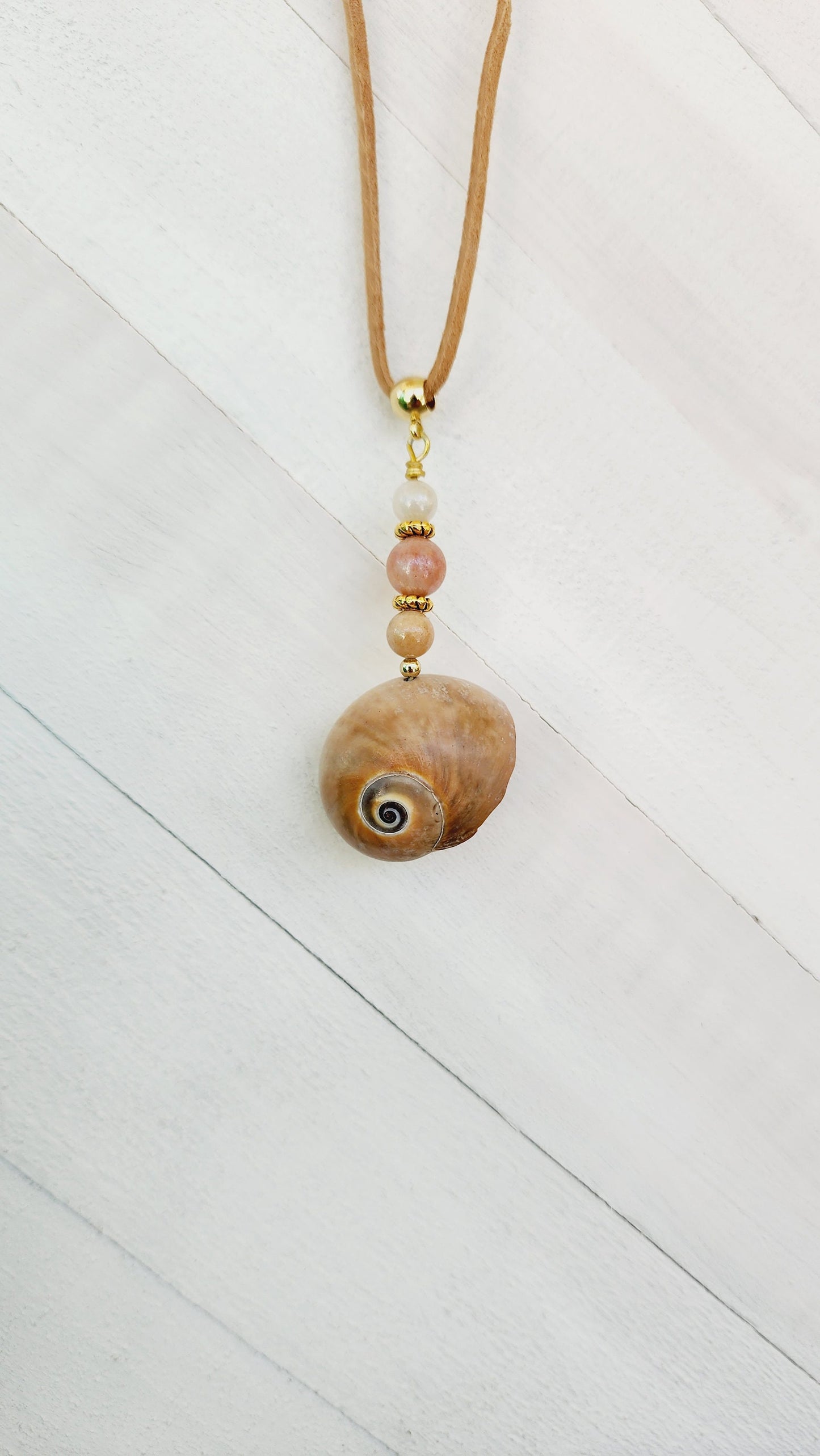 Genuine handmade shark eye moon snail pendant, accented with semi- precious sun stone beads. Tan suede 16" cord with 2" extender in gold.