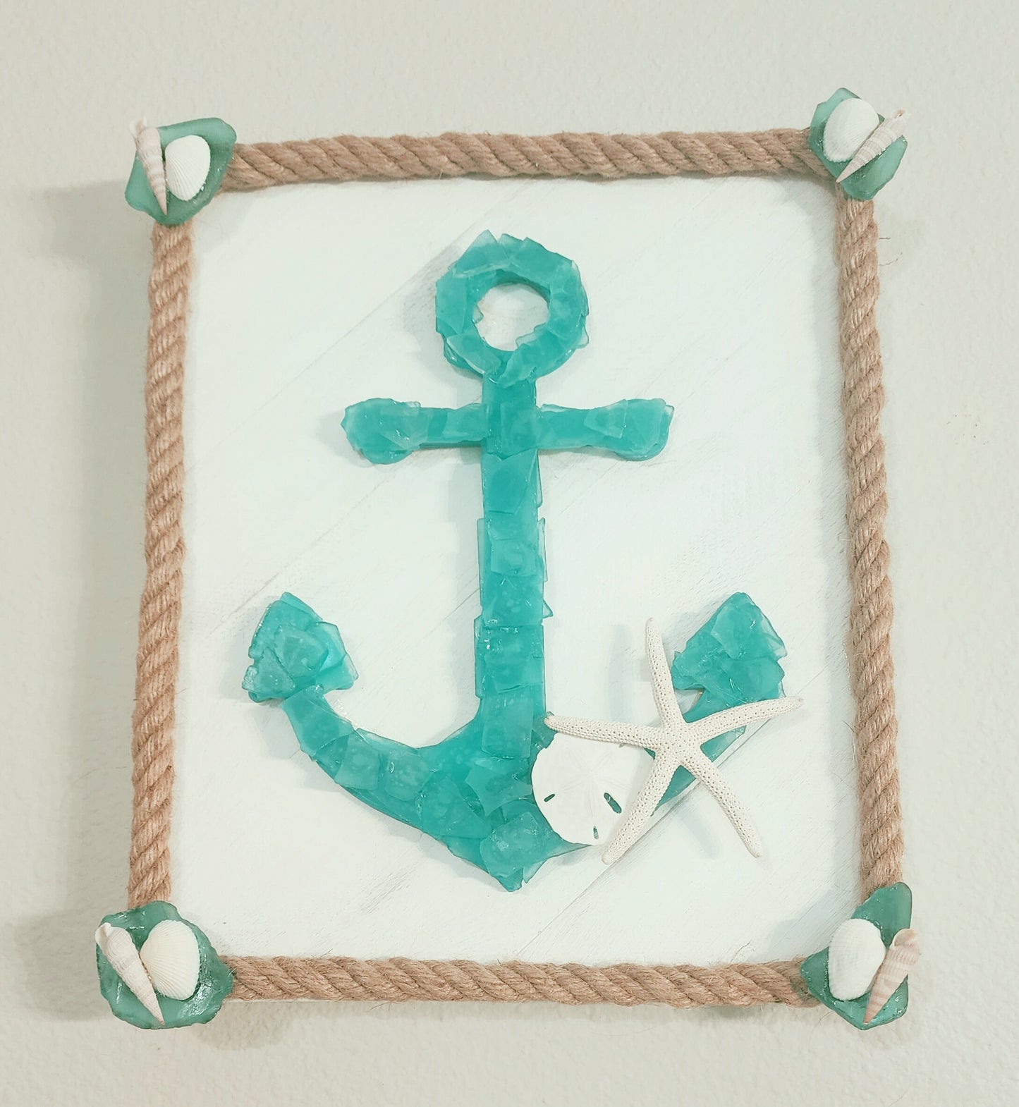 Sea glass anchor wall art in turquoise and white, surrounded with nautical jute rope, accented with a sand dollar and starfish.