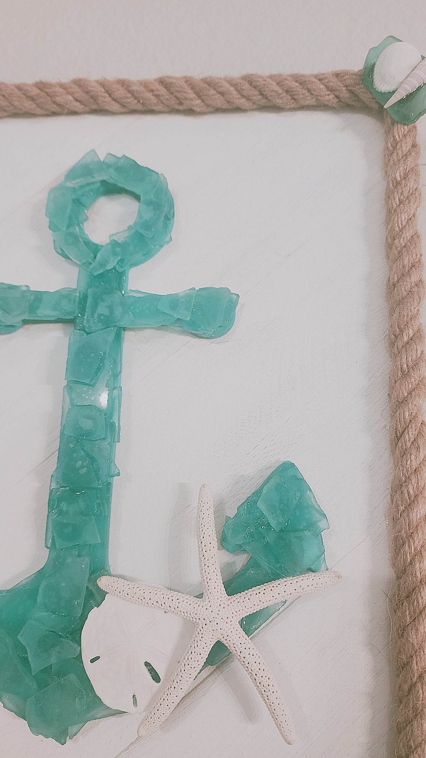 Sea glass anchor wall art in turquoise and white, surrounded with nautical jute rope, accented with a sand dollar and starfish.