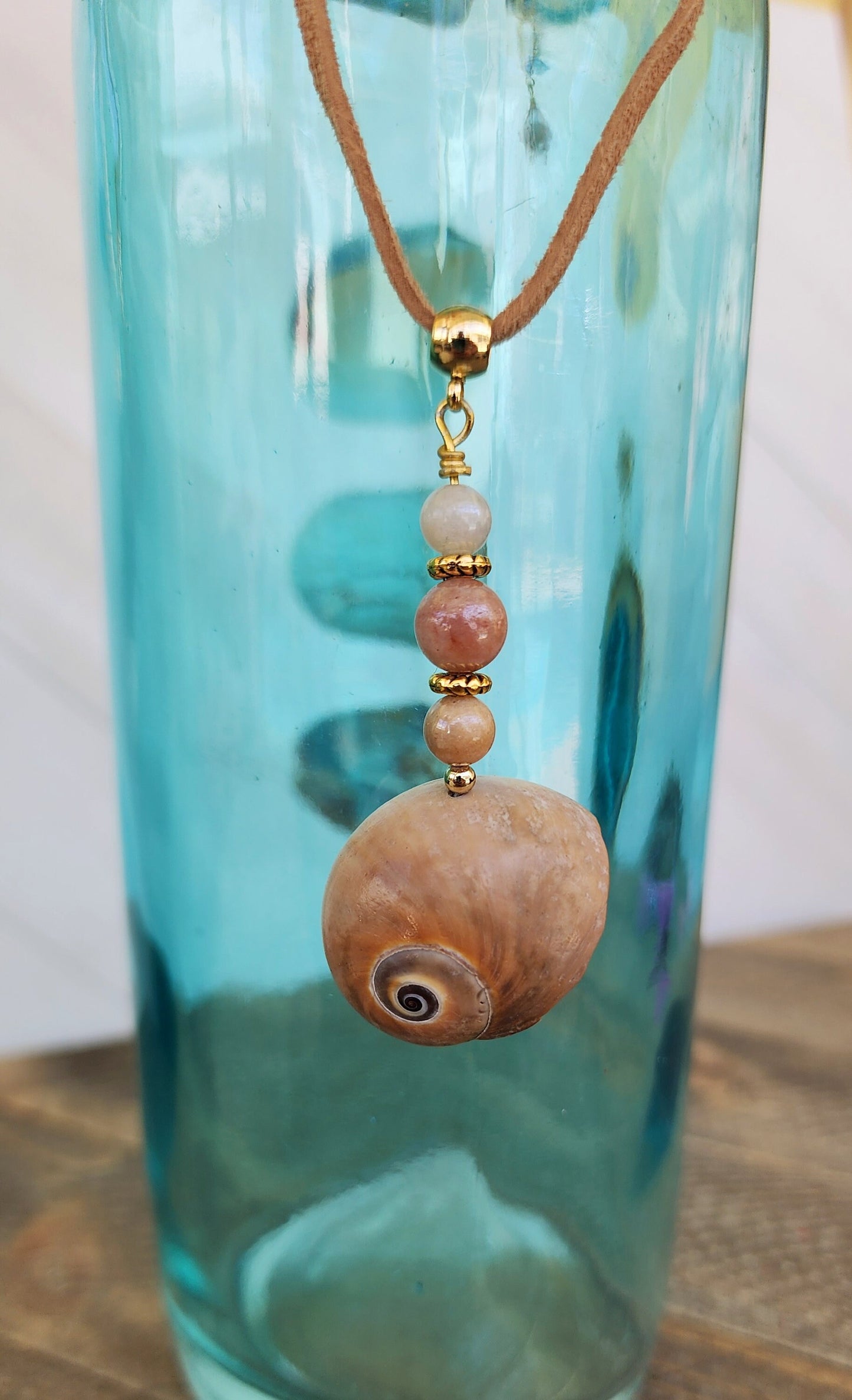 Genuine handmade shark eye moon snail pendant, accented with semi- precious sun stone beads. Tan suede 16" cord with 2" extender in gold.