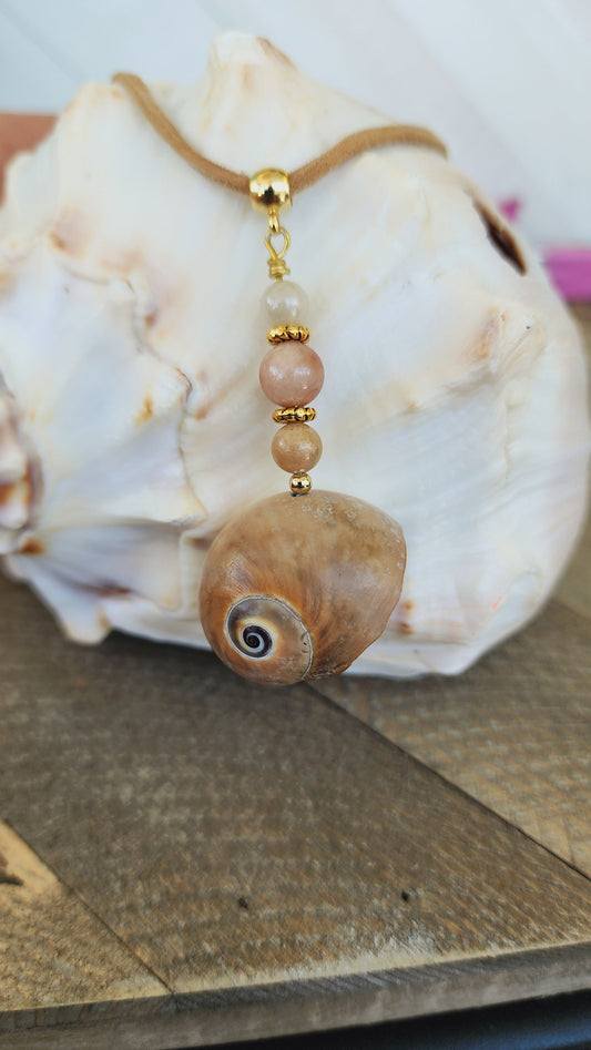 Genuine handmade shark eye moon snail pendant, accented with semi- precious sun stone beads. Tan suede 16" cord with 2" extender in gold.