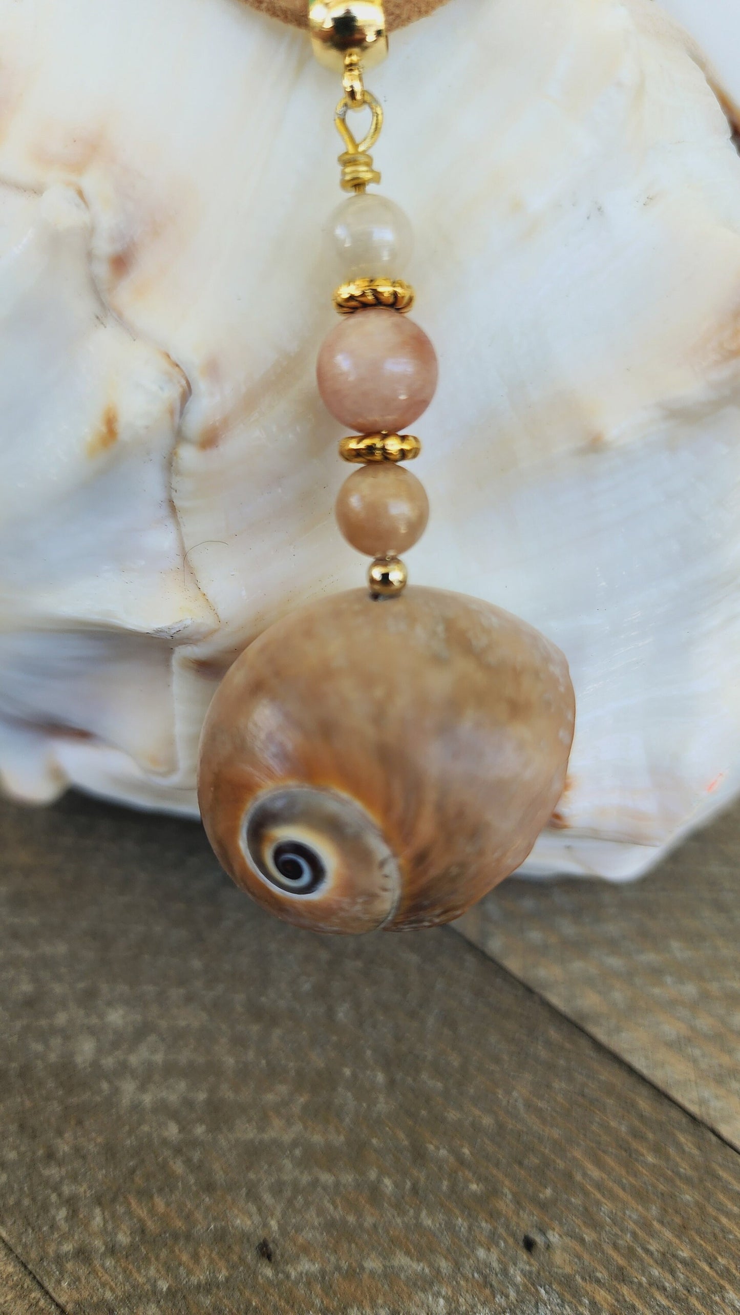 Genuine handmade shark eye moon snail pendant, accented with semi- precious sun stone beads. Tan suede 16" cord with 2" extender in gold.