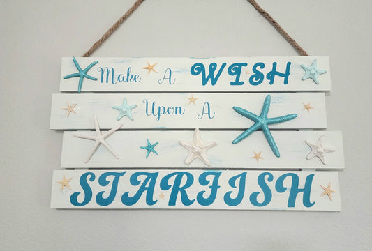 Handmade beach wall art "Wish upon a starfish" sign in varying shades of blues on a white hand painted and distressed wooden plaque.